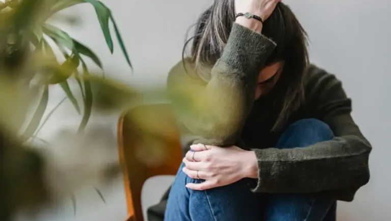Stressed young woman holding her head surrounded by green plants, symbolizing anxiety and natural healing